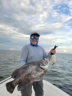 Person standing on a boat holding a large fish with water and cloudy sky in the background.